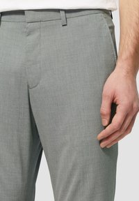 Hellgraue, maßgeschneiderte Hose mit glatter Textur, die ein schlankes Design, eine flache Vorderseite und seitliche Taschen aufweist. Gürtelschlaufen sind an der Taille sichtbar.