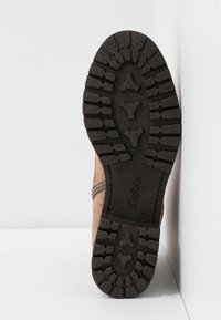 Semelle extérieure en caoutchouc noir avec des rainures profondes sur une botte beige, affichant le nom de la marque "Gabor" et un motif de grip texturé.