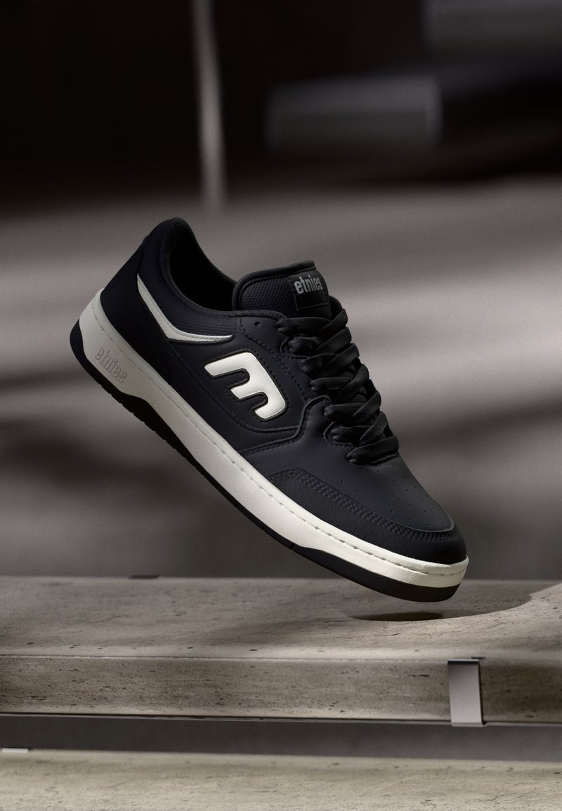 Μαύρο sneaker με υφή, λευκές λεπτομέρειες και έντονο λογότυπο στο πλάι. Διαθέτει σχέδιο με κορδόνια και μαλακό κολάρο.