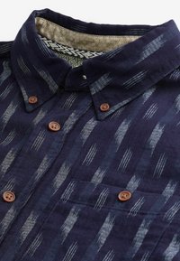 Marineblauw overhemd met knopen, voorzien van een gestructureerd patroon van lichte en donkere strepen, met bruine knopen en een kraagvoering met een patroon.