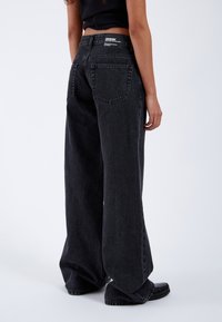 Wide-leg black denim jeans with a high waist, raw hem, and two back pockets. Features a branded waistband label.