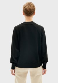 Čierny sweatshirt s okrúhlym výstrihom, raglánovými rukávmi a rebrovanými manžetami. Mäkka textúra, voľný strih a bezšvový dizajn chrbta.
