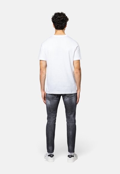 Witte korte mouwen t-shirt, grijze versleten slim-fit jeans en witte sneakers met zwarte accenten, gezien van achteren.