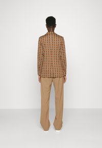 Bruine blazer met een patroon in een ruitdesign, gecombineerd met beige broek. De blazer heeft een gestructureerde stof en een licht getailleerde pasvorm.