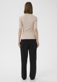 Beige vroubkovaný top s krátkým rukávem spárovaný s černými širokými kalhotami. Hladká textura, těsný střih s kulatým výstřihem a viditelnými švy.