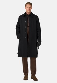 Melnas vilnas virsjakas ar apkakles kaklu, piecu pogu aizdari un sānu kabatām. Uzvilkts virs brūna krekla un brūnajiem biksēm, ar cimdiem.