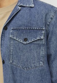 Denim jacket in medium blue met een voorzak en donkere knopen. Beschikt over een klassieke kraag en textuurstof.