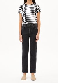 T-shirt rayé noir et blanc, jeans noirs taille haute, et chaussures slip-on beige clair. Coupe classique droite, manches retroussées, accent simple.