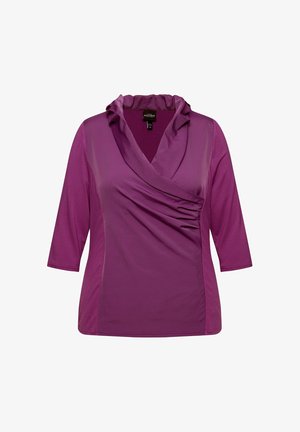 Lila Oberteil mit Dreiviertelärmeln, das einen drapierten Wasserfallkragen und seitliche Raffung aufweist. Geschmeidiger Stoff mit einem leichten Glanz.