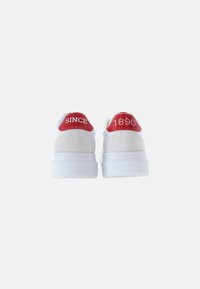 Sneaker bianche con dettagli in suede, linguette rosse sul tallone con la scritta "SINCE" e "1890." Suola spessa in gomma e texture liscia.
