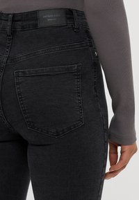 Črne denim hlače srednjega pasu, z zadnjim žepom in subtilnim šivom. Oznaka "popolne hlače" vidna na pasu.