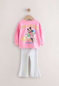 Lyserød sweatshirt med teksten "THE CREW" og tegneseriefigurer på ryggen, kombineret med grå udvidede bukser. Glat stof, afslappet design.