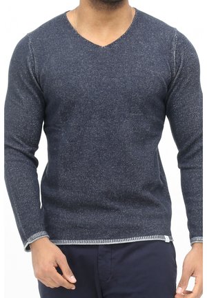 Uomo che indossa un maglione a V blu navy dalla trama strutturata con polsini e orlo a contrasto, abbinato a pantaloni scuri.