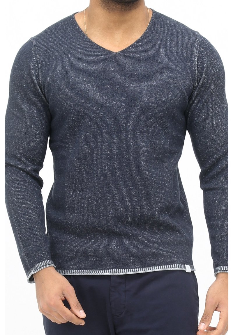 Homme portant un pull en V bleu marine texturé avec des poignets et un ourlet contrastants, associé à un pantalon sombre.