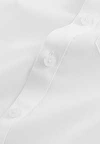 Witte button-up blouse van een gladde stof met een overlappende knoopsluiting en heldere plastic knopen. Eenvoudig, klassiek ontwerp zonder patronen.