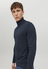Pulover în gât de culoare albastru marin, dintr-un tricot moale și texturat. Design ajustat cu manșete și margini ribbate, și umeri fără cusături pentru linii curate.