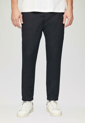 Dunkelgraue, schmal geschnittene Hosen aus strukturiertem Stoff, kombiniert mit weißen Sneakers. Die Hosen haben ein klares Design mit minimal sichtbaren Nähten.