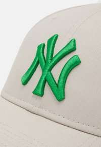 Gorra de béisbol beige con un acabado texturizado, que presenta un gran logo bordado en verde con la letra "NY" en la parte frontal.