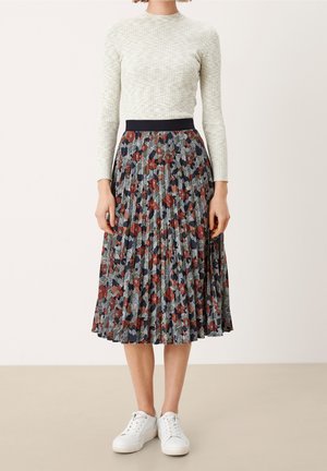 Hvid langærmet top med tekstureret mønster, parret med en plisseret midi-nederdel med et blomsterprint i rød, marineblå og grøn. Hvide sneakers.