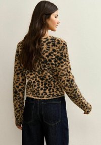 Pluizige leopardprint trui in beige en zwart met lange mouwen, ronde halslijn en een cropped pasvorm, gecombineerd met donkere denim jeans.