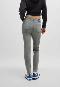 Harmaat farkut, joissa on kapeat lahkeet, taka-taskut ja sininen brändi vyötärö, yhdistettynä sinisiin ja valkoisiin tennareihin.