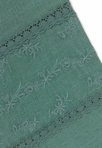 Tela color verde azulado con patrones florales bordados y ribete de encaje en el mismo tono verde azulado.