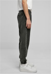 Mørkegrå joggers med elastisk talje, sidelommer og tætsiddende manchetter, parret med hvide sneakers på en neutral baggrund.