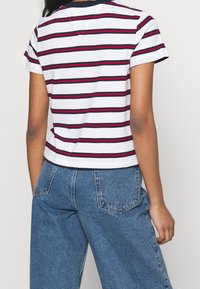 Camiseta de manga corta a rayas en blanco, azul marino y rojo. Tejido suave, escote redondo, diseño corto. Se lleva con pantalones de mezclilla claros de cintura alta.