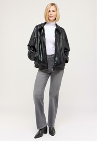 Schwarze Leder-Fliegerjacke mit Reißverschluss, kombiniert mit grauen geraden Jeans und schwarzen spitzen Ankle Boots. Glatte, glänzende Textur.