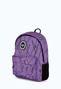 Violetti reppu, jossa on mustia sydänkuvioita, etutasku ja pyöreä logotarra. Varustettu säädettävillä olkaimilla ja ripustuslenkillä.