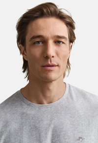 Siva bombažna majica z okroglim izrezom, na prsih majhen logotip. Mehka tekstura in sproščen dizajn, primeren za vsakodnevno nošenje.