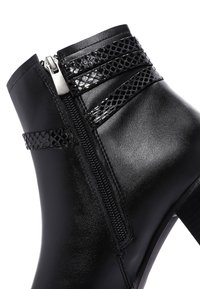 Bottines noires avec une finition en cuir lisse, présentant des sangles décoratives, une fermeture éclair sur le côté et un accent texturé pour plus de détails.