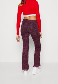 Punainen pitkähihaisen crop-top, jossa on valkoinen raitavyötärö, yhdistetty korkeavyötäröisten, leveälahkeisten tummanviolettien housujen kanssa, joissa on vaaleanpunainen abstrakti kuvio.