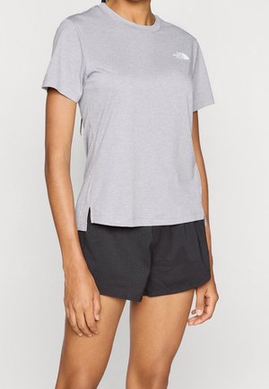 Osoba ubrana w jasnoszarą koszulkę z krótkim rękawem z logo The North Face oraz czarne teksturowane szorty, stoi na jednolitym tle.