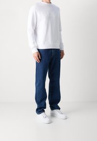 Vit crew-neck sweatshirt med präglad "BOSS"-logotyp, i kombination med löst sittande blå denimjeans och vita sneakers. Enkelt, avslappnat klädval.