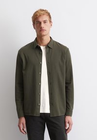 Olive green button-up shirt made of soft fabric, featuring a classic collar, long sleeves, and a straight cut. Underneath, a white T-shirt is visible.