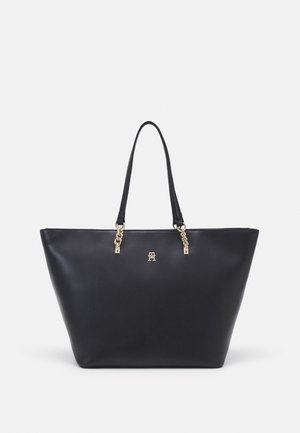 Black leather tote bag with gold chain details on handles and a small gold logo emblem centered on the front.