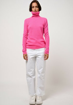 Roze coltrui met een zachte textuur en een slim fit ontwerp, gecombineerd met witte wijde broek en witte sneakers.