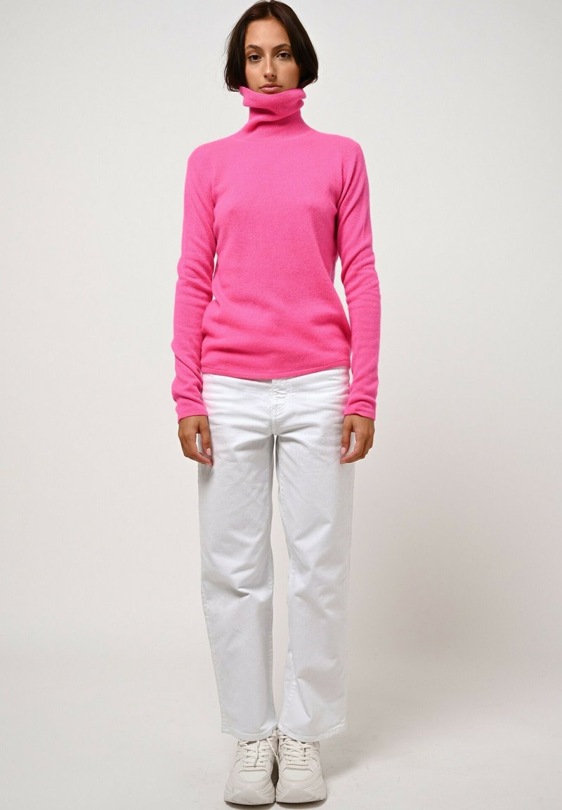 Maglione a collo alto rosa con una texture morbida e un design aderente, abbinato a pantaloni bianchi a gamba larga e sneakers bianche.