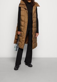 Brązowa ocieplana kamizelka z kapturem, z zamkiem błyskawicznym z przodu i zatrzaskami. Nosi ją się na czarną bluzkę, w zestawieniu z czarnymi spodniami i butami.