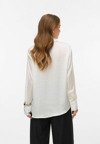 White, long-sleeve blouse with a smooth, shiny texture; features buttoned cuffs with metallic accents; back view shows a relaxed fit.
