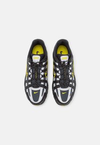 Paire de baskets Nike noires, blanches et jaunes avec un design à lacets et logos jaunes Nike sur la languette et les orteils, vues de dessus sur fond blanc.