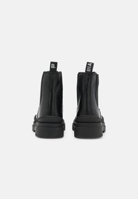 Czarne botki za kostkę z gładką syntetyczną cholewką, elastycznymi panelami bocznymi i grubymi gumowymi podeszwami. Posiadają pętle do ciągnięcia z kontrastowym białym napisem.