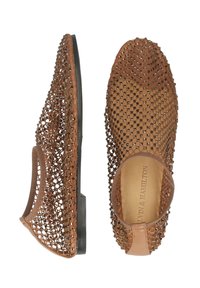 Bruna, flätade platta skor med perforerat mönster, öppna sidor och en solid svart sula. Har en texturerad yta och elastiskt hälband.