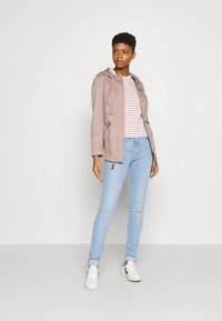 Lys rosa hettejakke, hvit og rosa stripete skjorte, lyseblå jeans, hvite joggesko. Enkel design med snøring og lommer.