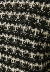 Tissu texturé avec un motif pied-de-poule noir et blanc, comportant des fils métalliques, créant un effet scintillant à la surface.