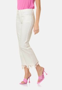 Jeans blancos de cintura media con dobladillo deshilachado, combinados con tacones rosa brillante atados, junto con una camiseta ajustada rosa.