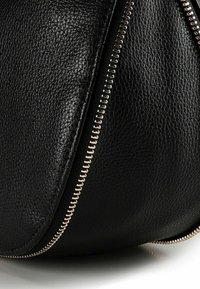 Zwart leren tas met een gestructureerd oppervlak, voorzien van een goudkleurige ritssluiting langs de naad voor een veilige sluiting en extra detail.