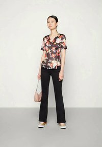 Blusa em tecido escuro com estampa floral, apresentando mangas curtas e cintura ajustada. Combinada com calças pretas largas e ténis brancos.