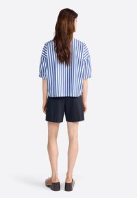 Haut à manches courtes rayé bleu et blanc, coupe décontractée, assorti à un short noir et des chaussures à plateforme marron, vu de l'arrière.